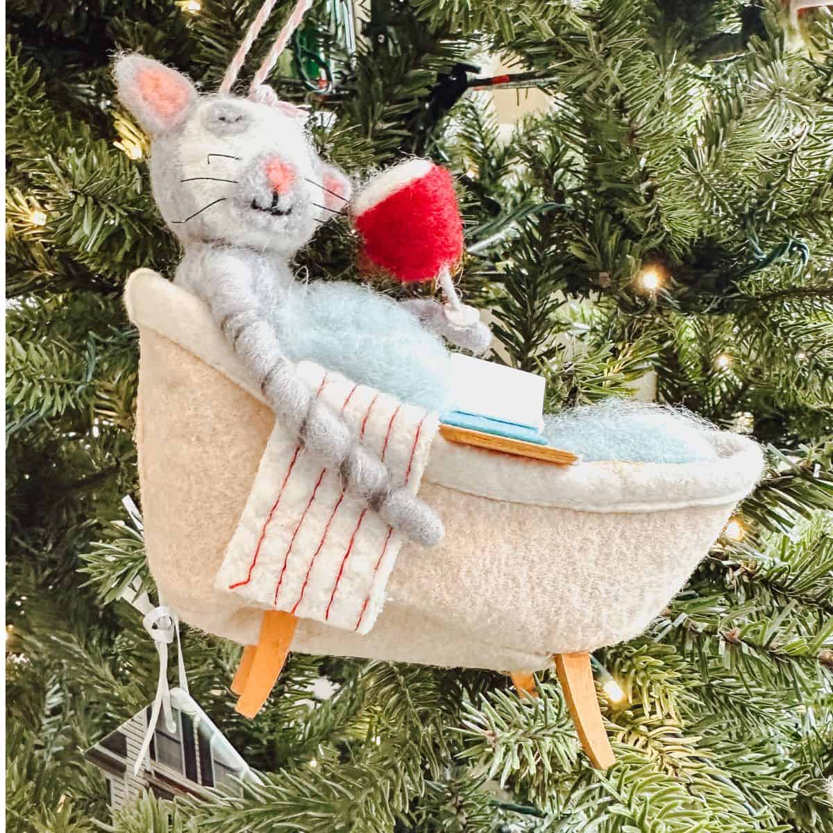 ornament of cat reading in the bath with wine in front of a christmas tree.