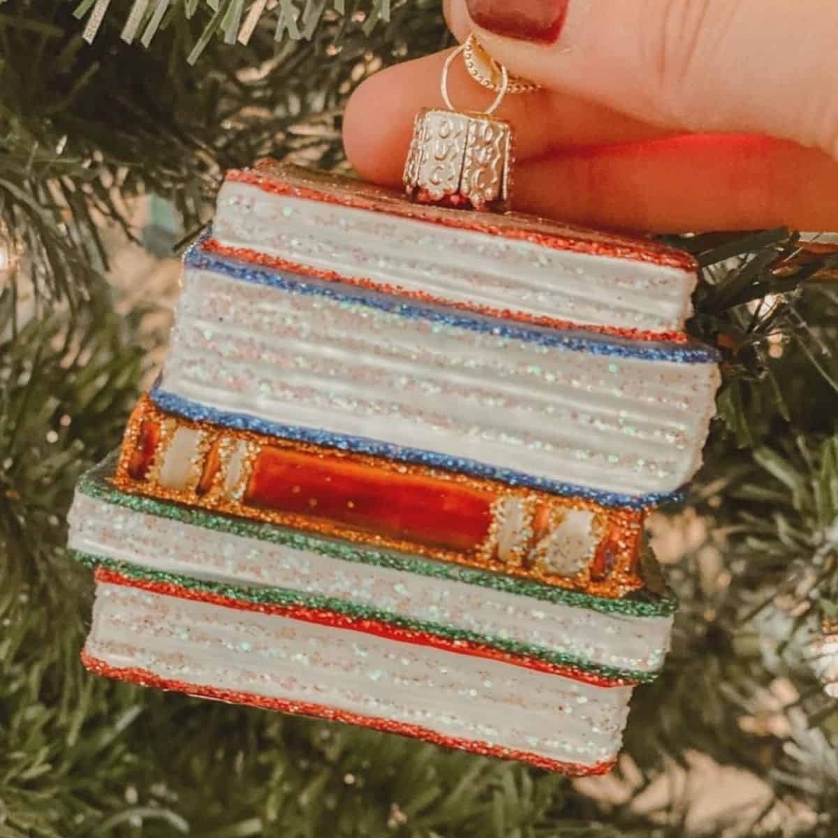 blown glass bookstack ornament in front of christmas tree.