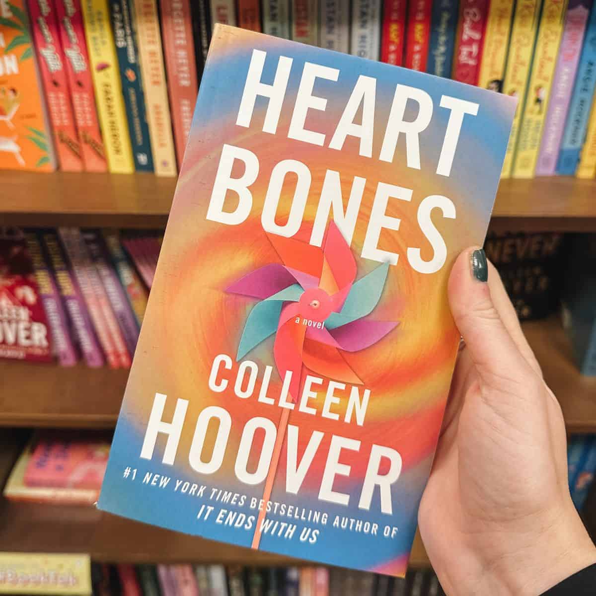 heart bones by colleen hoover in front of bookshelves.