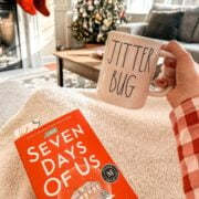 woman reading a book and drinking hot chocolate in front of a christmas tree.