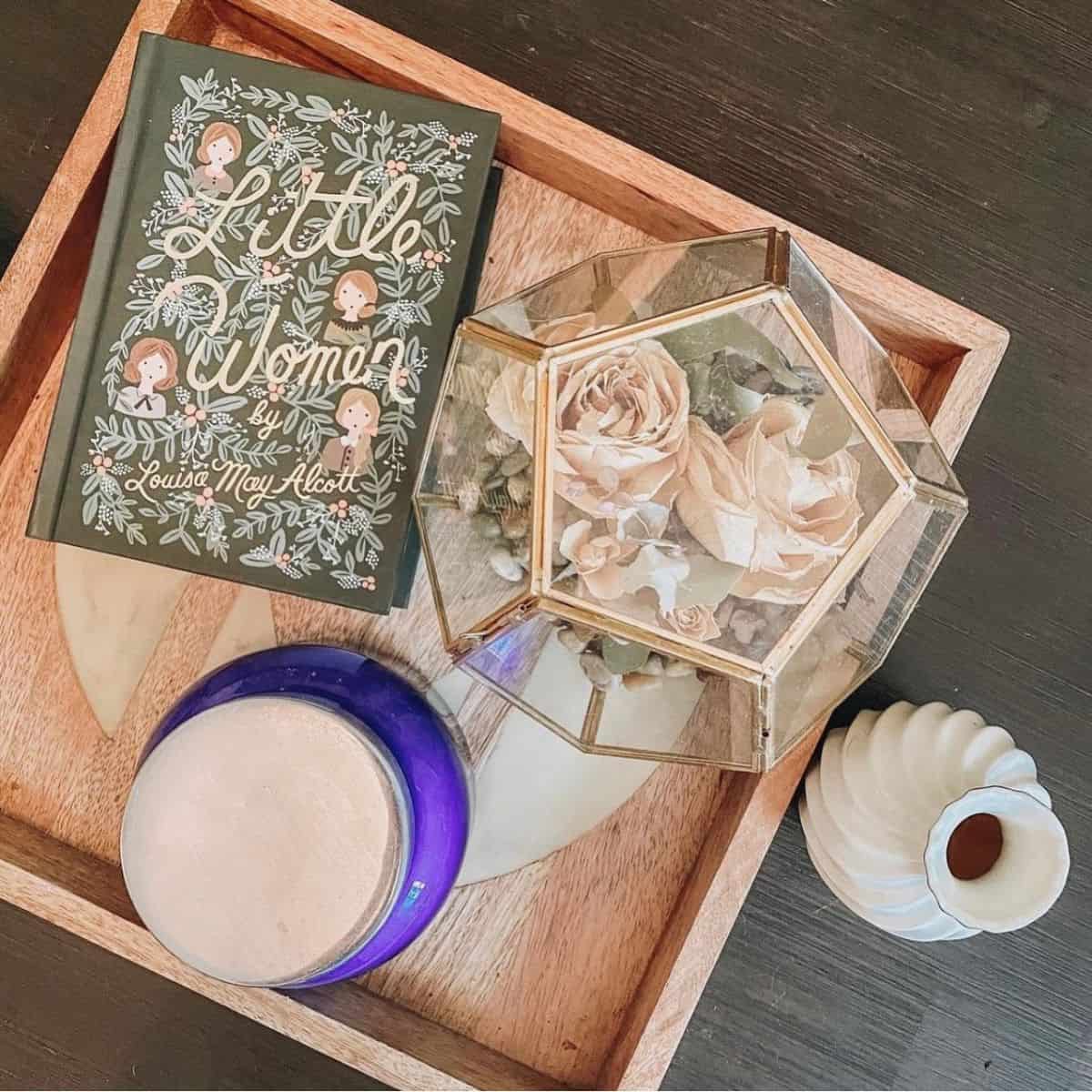 little women by louisa may alcott on a tray with flowers and candles.