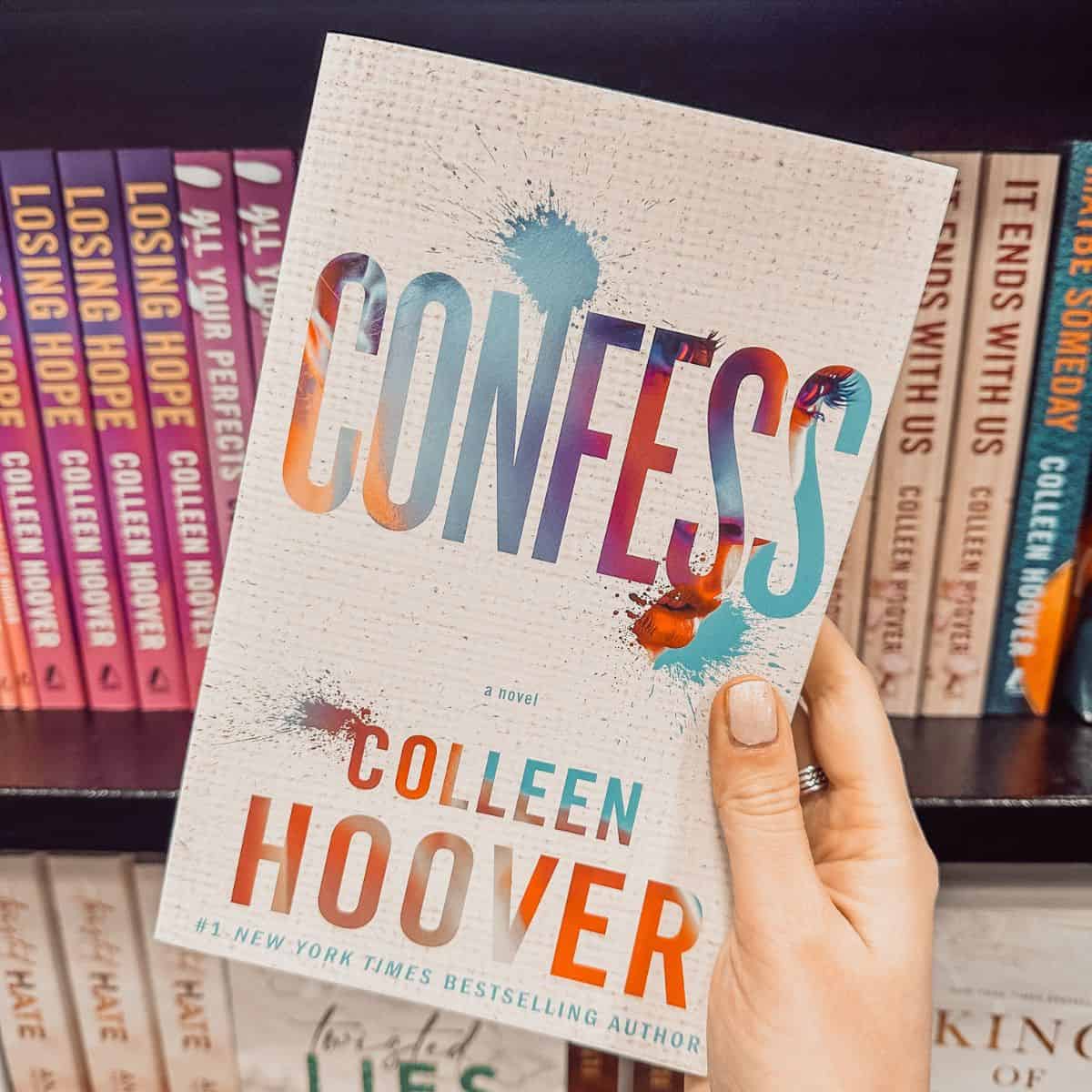 Confess by Colleen Hoover held in front of a bookshelf with other Colleen Hoover books.