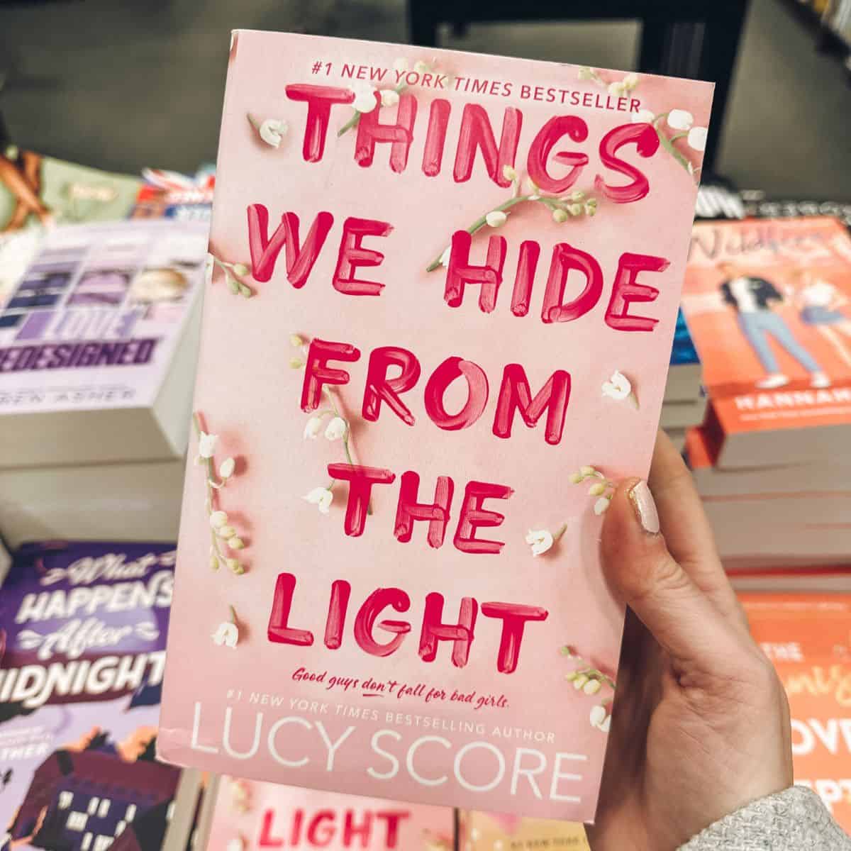 Things we hide from the light by Lucy score held in front of a table of books.