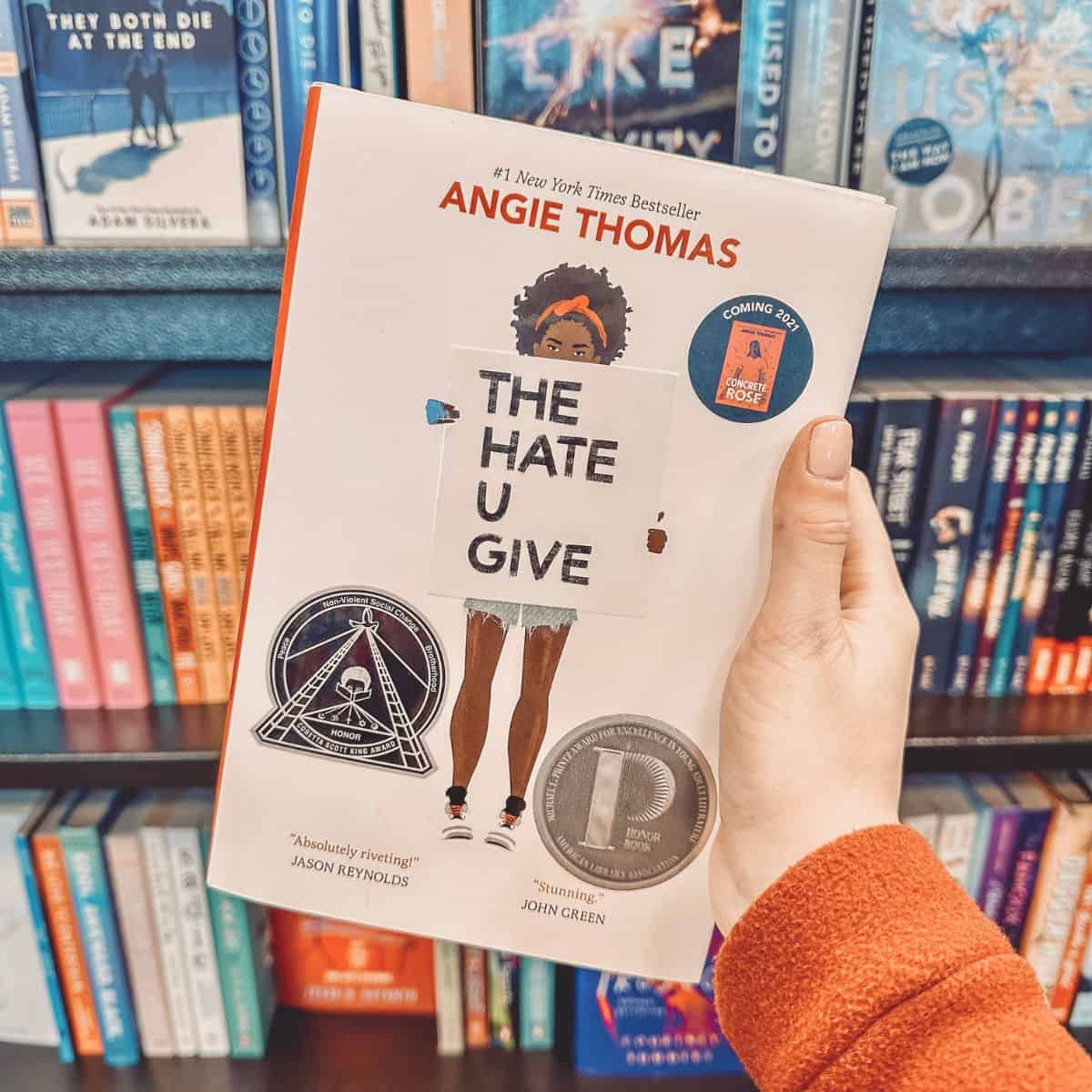 The hate you give by Angie Thomas in front of bookshelves.