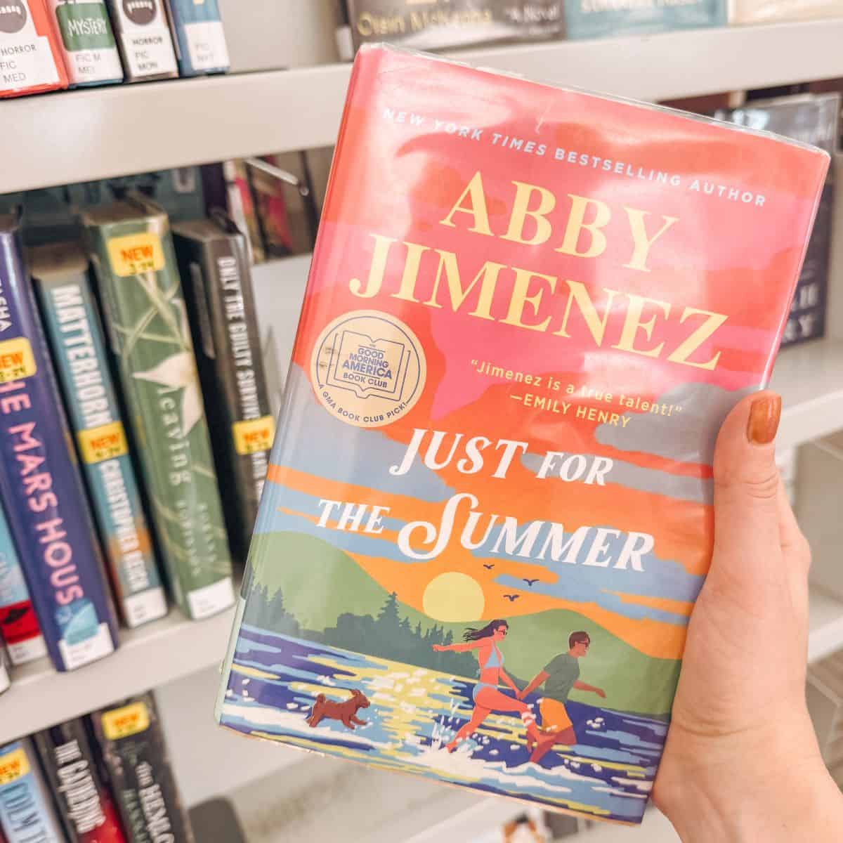 just for the summer by abby jimenez in front of bookshelves.