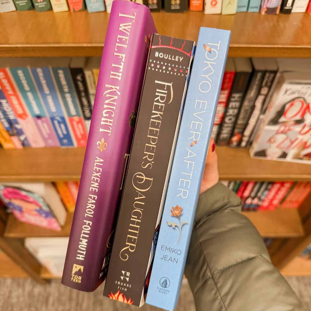 person holding reese witherspoon ya books in front of bookshelf.